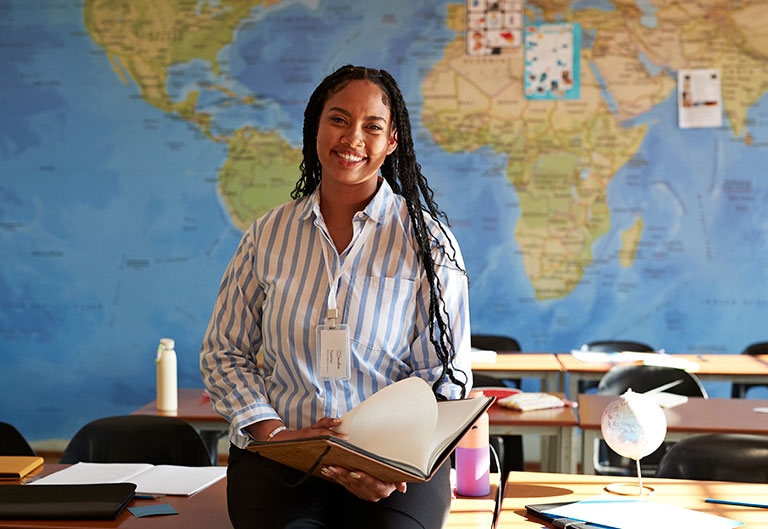 African American Woman standing at front of classroom with world map behind her