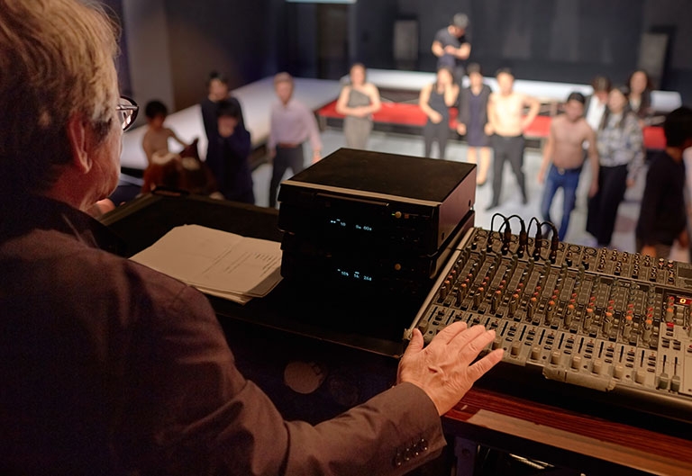 Art director working at sound board with actors on stage