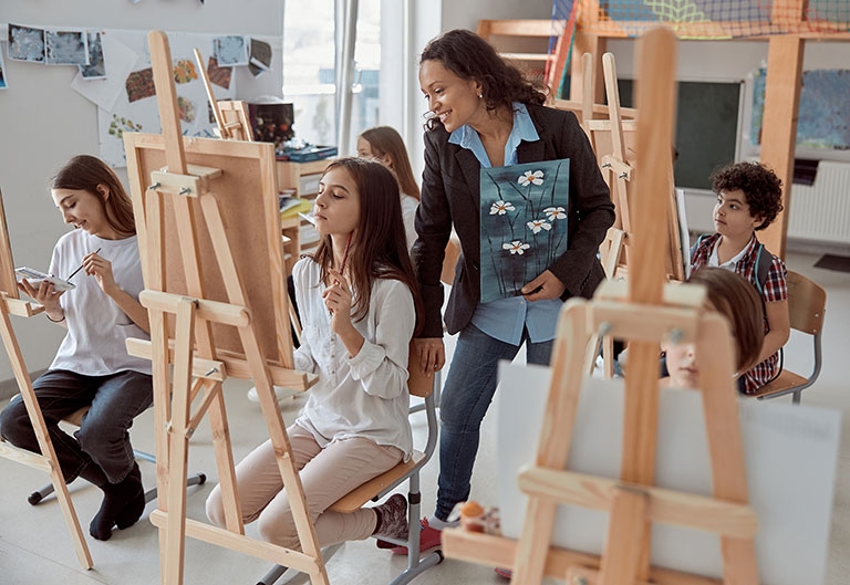 Art teacher instructing students as they paint at easels