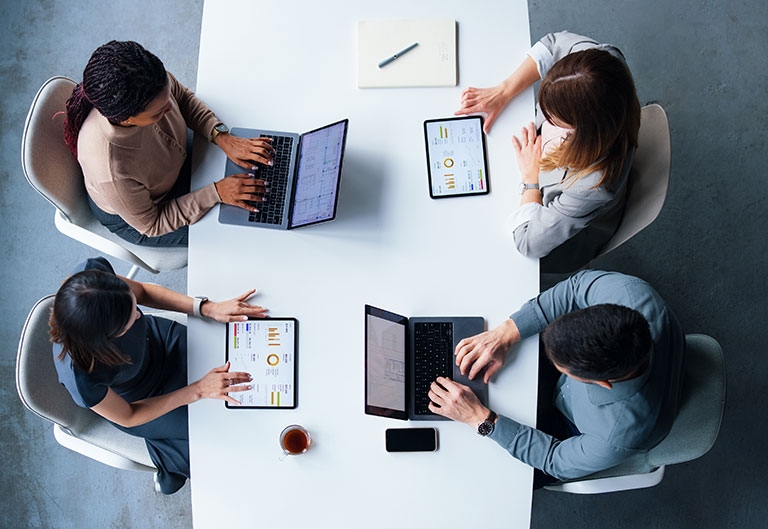 Four co-workers at table, with statistics on their laptops