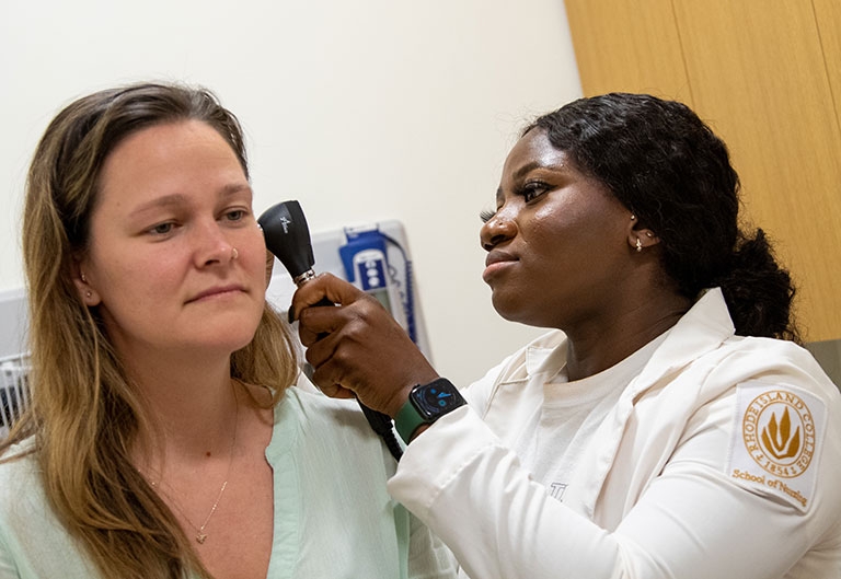 Nursing student looking into patient's ear with otoscope