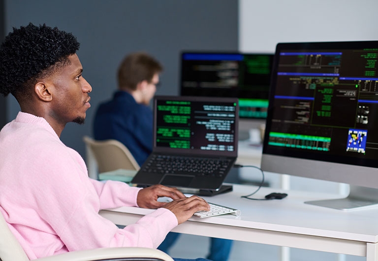 People working in space with many computer monitors, code on the screens