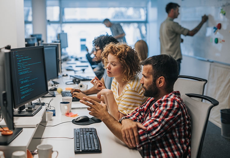 People working in a start-up type workplace, at computers and a white board