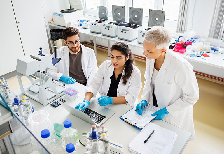 Three chemists working in lab together at a table with equipment