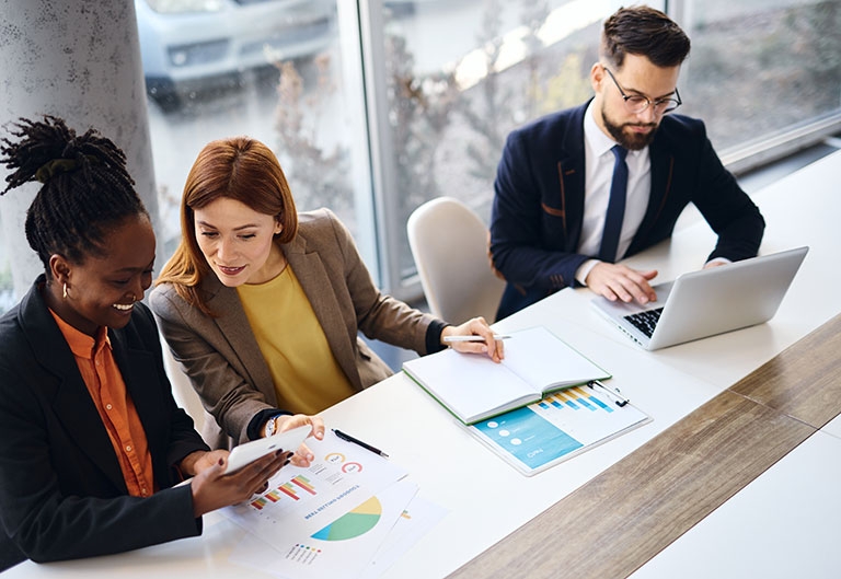 Three people working in office with laptop, tablet, charts, notebook