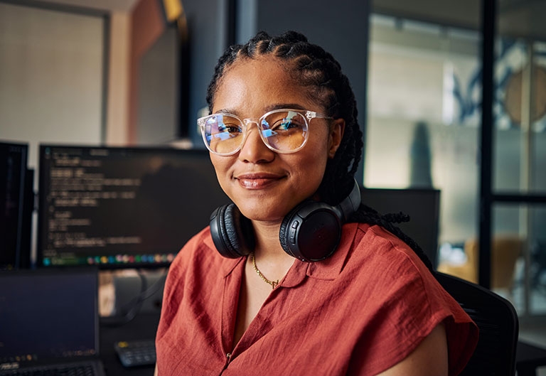 Woman at multiple monitors showing code, wearing headphones around neck