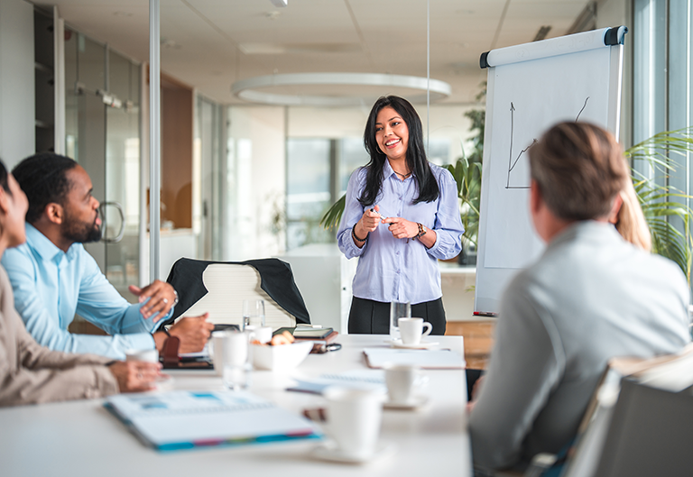 Woman leading a meeting, drawing a chart with others listening at table