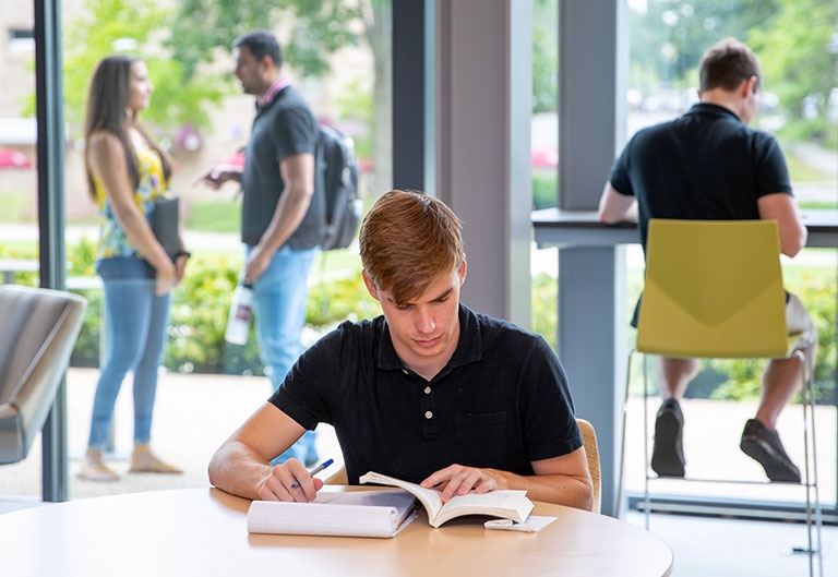 Student studying in lobby of Craig Lee Hall by windows