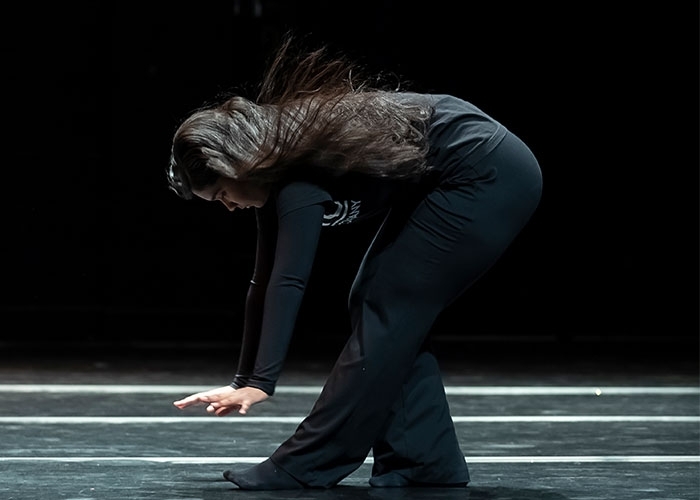 Dance major, Andreina Mendoza in motion on stage, reaching downward, hair flowing