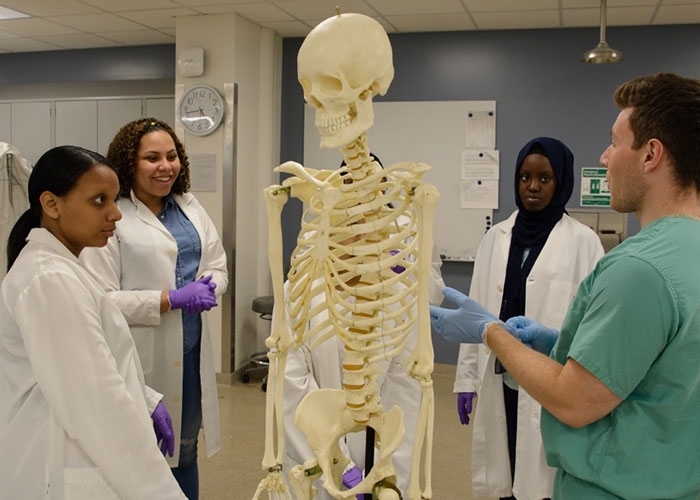Ambar Mella in lab with students, standing near skeleton