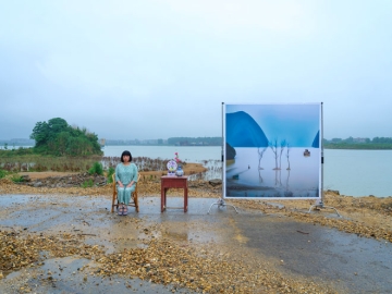 Photograph of a woman seated next to an AI-generated image of a landscape