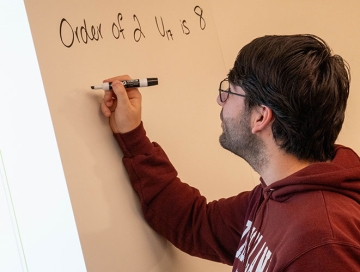 RIC male student in RIC sweatshirt works out a math equation on a whiteboard