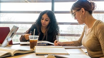 Math students working together at a table with notebooks, laptop, coffee