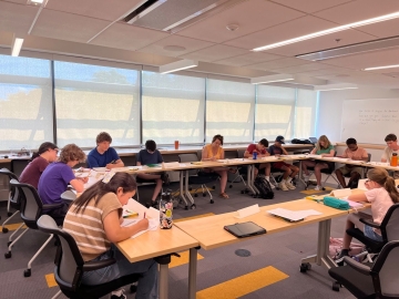 Children of different ages writing around tables forming a rectangle