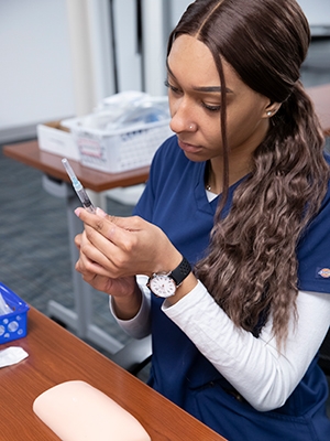 Medical Assistant student in scrubs, with needle.