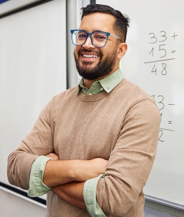 Elementary school teacher smiling, standing in front of whiteboard containing addition problems