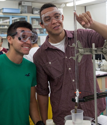 Two students in googles smiling as they work in chemistry lab with equipment