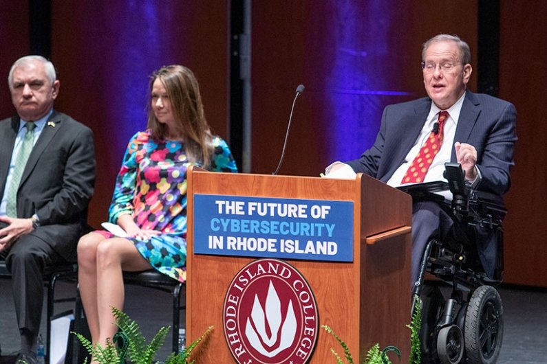 U.S. Representative Jim Langevin at podium, with Director of the Cybersecurity and Infrastructure Security Agency (CISA) Jen Easterly and Senator Jack Reed 