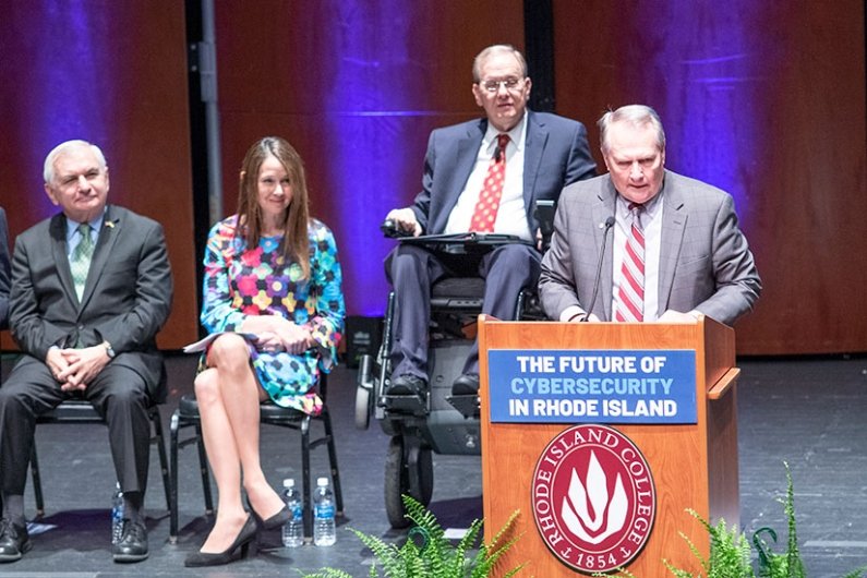 President Warner at podium with (from left to right) Senator Jack Reed, Director of the Cybersecurity and Infrastructure Security Agency (CISA) Jen Easterly, and U.S. Representative Jim Langevin at the launch of the Institute for Cybersecurity and Emerging Technologies