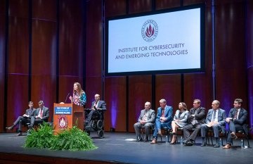 Speakers on stage at the Cybersecurity Institute launch with Jen Easterly speaking at the podium