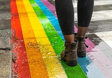 A pair of legs walks across a rainbow colored cross walk