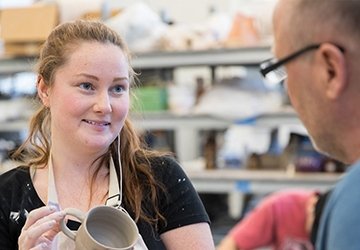 Art student working on pottery, with faculty looking at the work