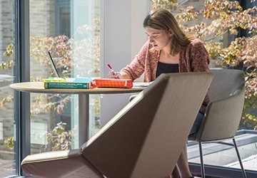 Student writing in the lobby of Craig Lee Hall, by windows