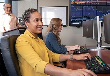 Two students in finance lab with professor in background