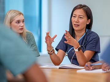 A small group of Nurse sit at a boardroom table as they meet to discuss patient cases