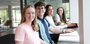 Four students together, smiling, in a sunny building lobby on RIC campus