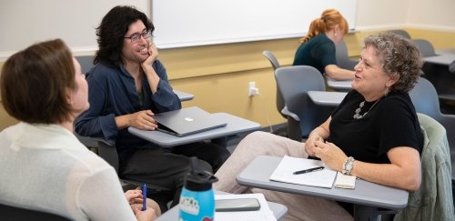 Staff and faculty at desks, talking happily