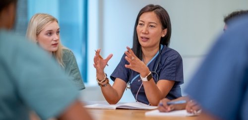 A small group of Nurse sit at a boardroom table as they meet to discuss patient cases