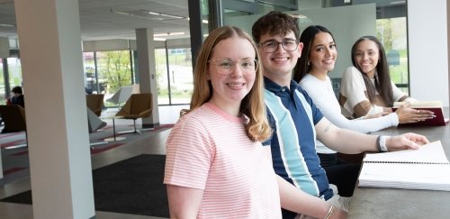 Four smiling students in sunny building lobby