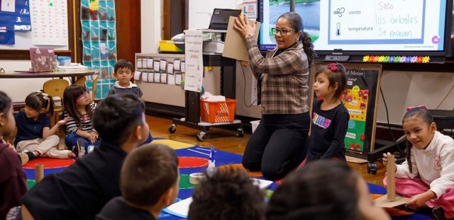 Pre-K-12 paraprofessional, Dolca Mendoza, teaching young students on rug