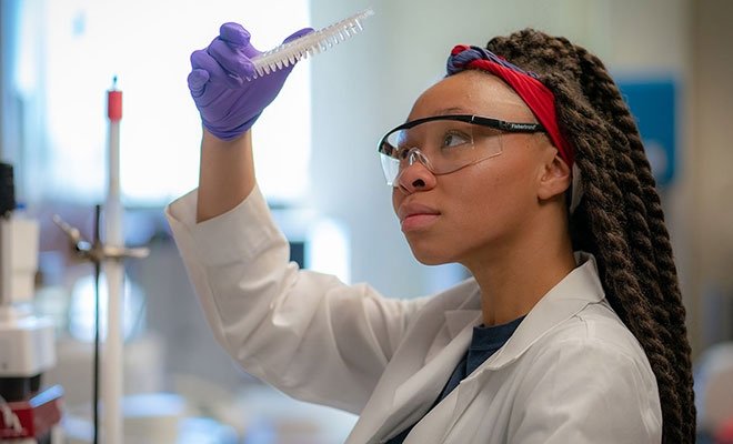 Biology student working in science lab in lab coat, with goggles, and looking at specimen