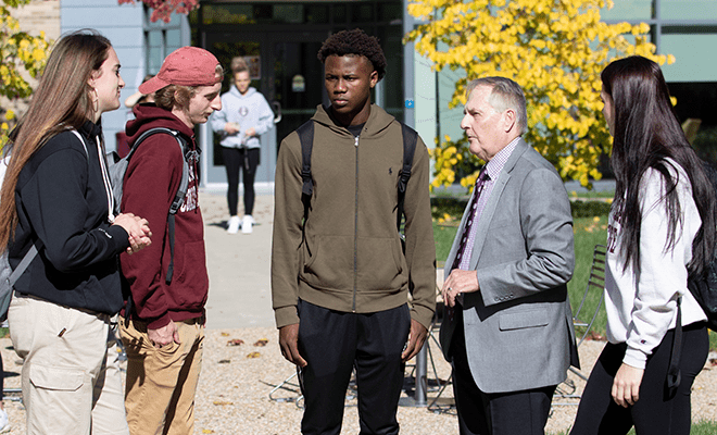 President Warner talking to a small group of students outside, on campus