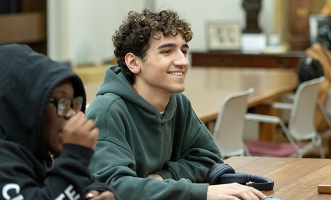 Male student sitting at table in class, smiling