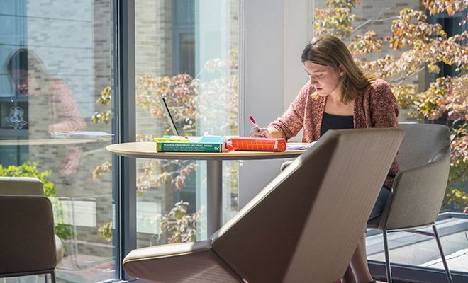 Student writing in lobby of Craig Lee Hall, by windows