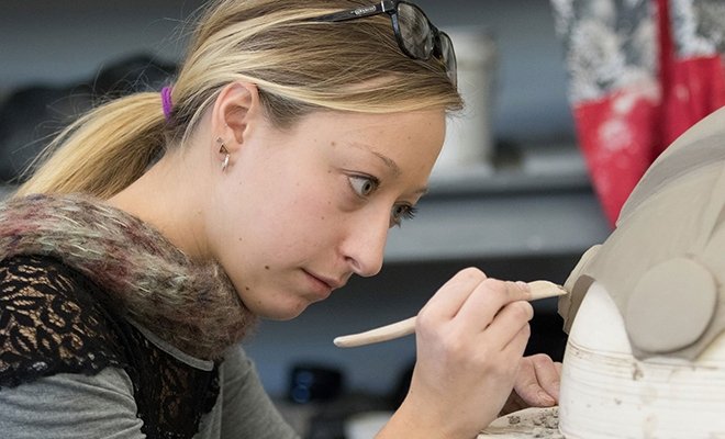 Student carefully shaping clay with a tool