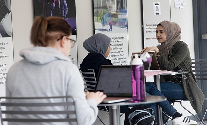 Students sitting at small tables with supplies, two wearing headscarves
