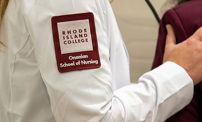Nursing student in white nursing coat with RIC Onanian School of Nursing badge on sleeve