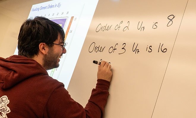 Student writing equations on white board in math class